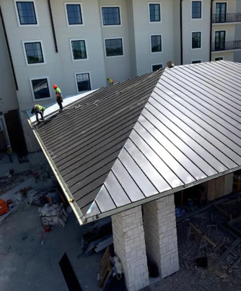 Crew installing standing seam metal roof panels on a commercial project in Lenox